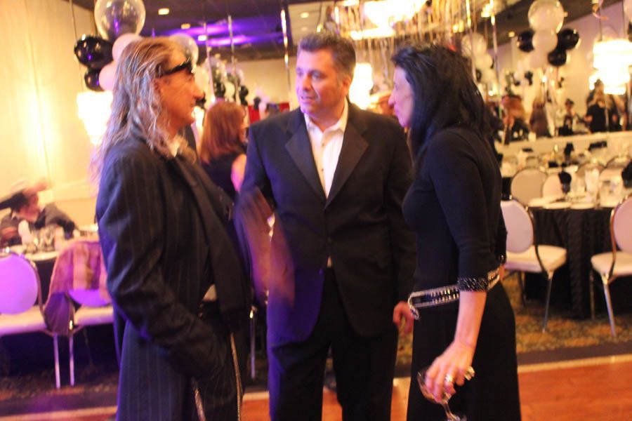 Three people conversing at a formal event, likely a gala. One wears a suit, others are in dresses.