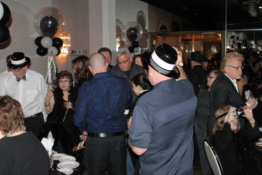 People in a crowded room at a party, wearing hats and surrounded by black and white balloons.