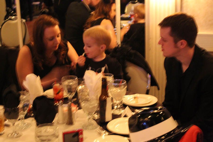 A family at a formal dinner table, the child eating a snack.
