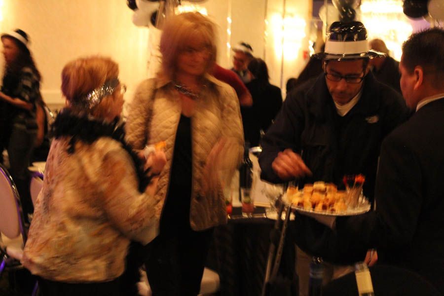 People at an event, one wearing a party hat, receiving food from a server.
