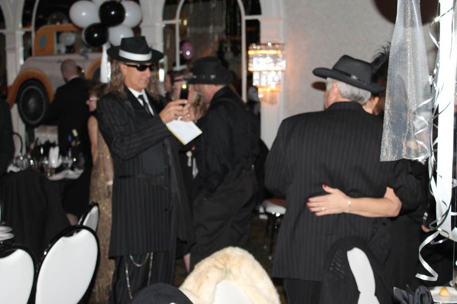 People in fedora hats at a party, one holding a drink, another dancing. Black and white decor.