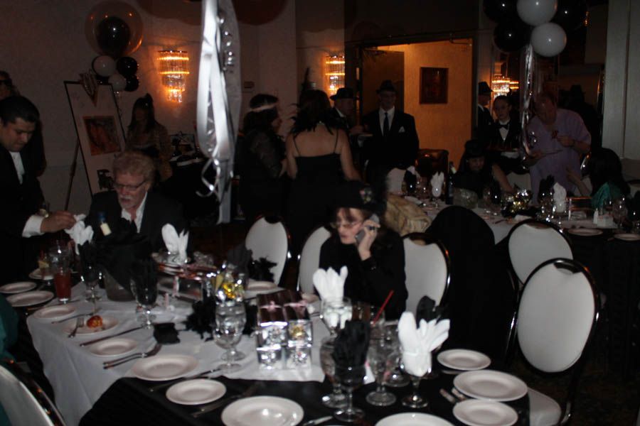 People at tables, a formal party. Black and white decor, some wearing masks.