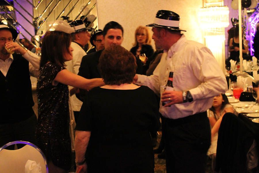 People in party hats at a gathering, one man holds a beer, gesturing as they celebrate.
