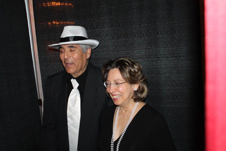 Man in fedora and suit with woman in black smiling, posing together.