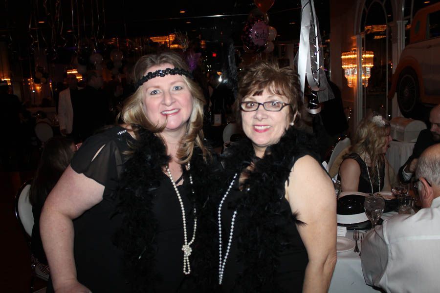 Two women in flapper attire, smiling at a party with decorations.