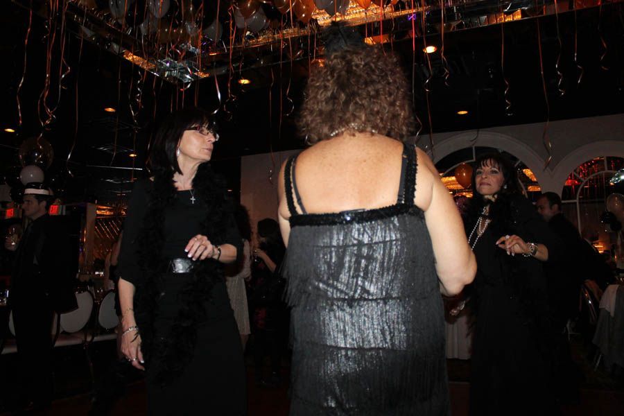 Three people in a dimly lit room, possibly dancing. Woman in black dress is center, two others are on the sides.