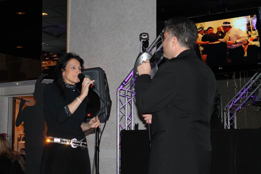 Two people singing into microphones on a stage with a screen in the background.