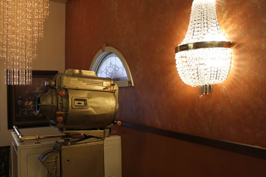 Gold film projector on a white box, set against a brown wall with ornate chandelier and small window.