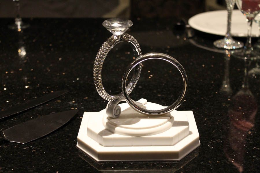 Diamond engagement ring and wedding band on a white stand, displayed on a black, speckled tabletop.