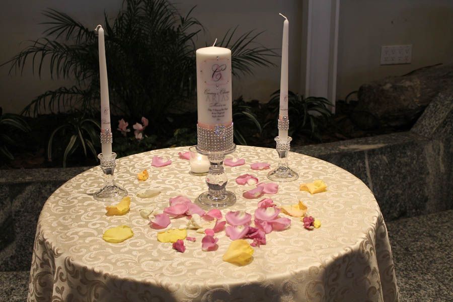 Wedding unity candle display with pink and yellow rose petals scattered on a table.