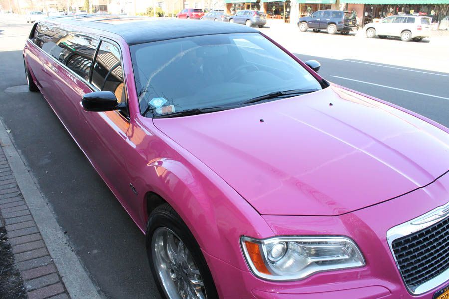 Pink Chrysler 300 limousine parked on a street with a black roof and chrome wheels.