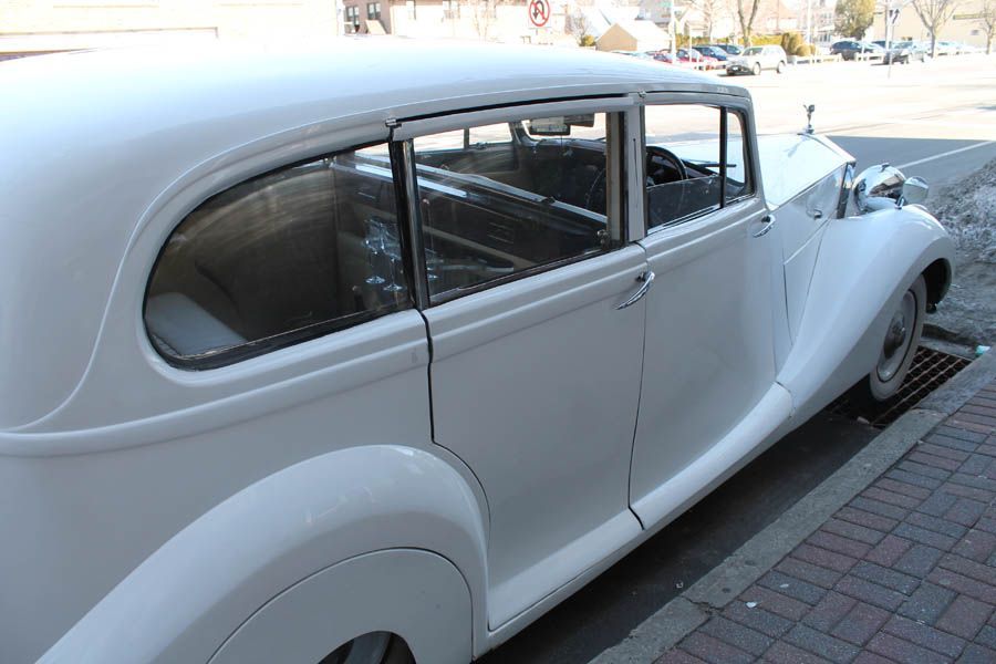 White vintage limousine parked on a street curb.