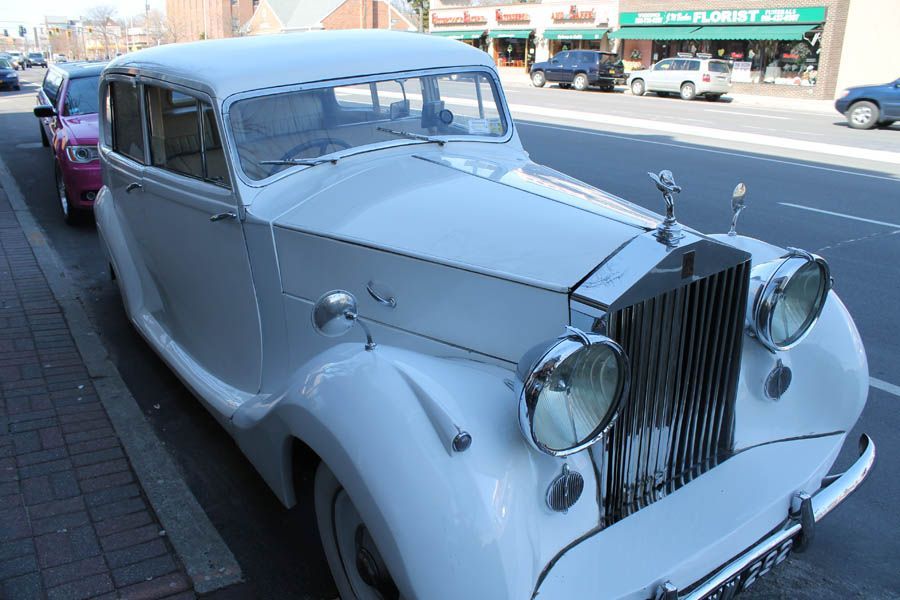 White vintage Rolls-Royce parked on a city street in front of shops.