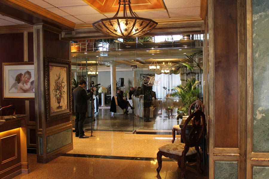 Hotel lobby with ornate doorway and mirror, a person filming, chair, and guests in the background.