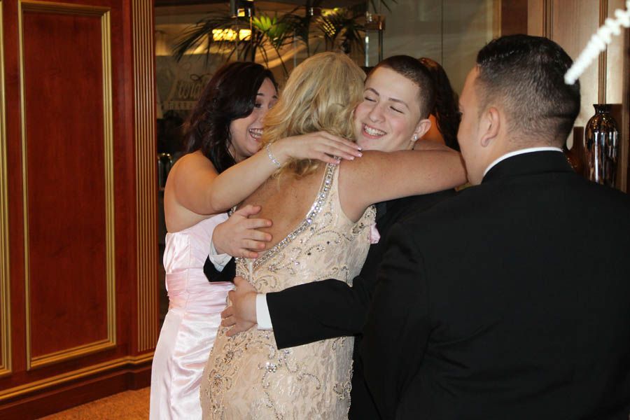 Group of people embracing, at event. One woman in sparkling dress, others in formal attire.