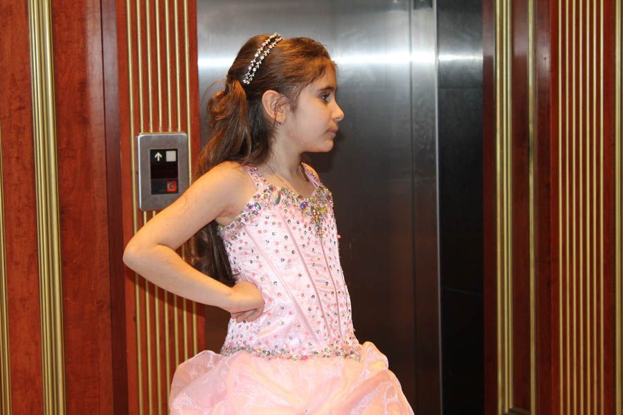 Girl in pink formal dress standing in an elevator, hand on hip.