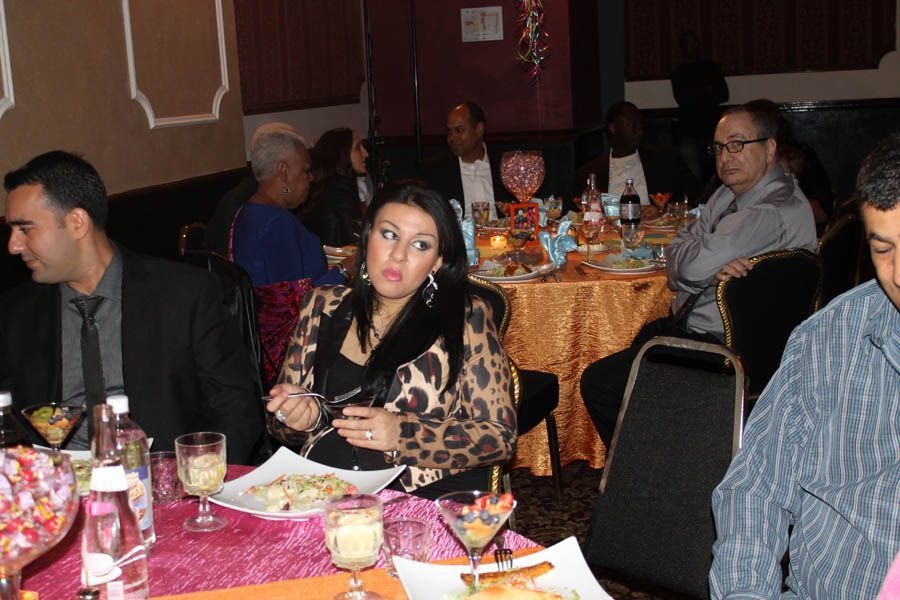 People seated at tables in a restaurant, eating and talking. One woman in leopard print jacket gestures.