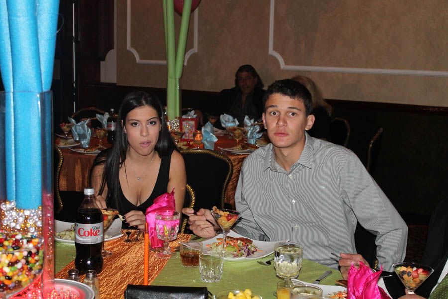 Woman and man at a table, both with surprised expressions, eating food. Restaurant setting, colorful decorations.