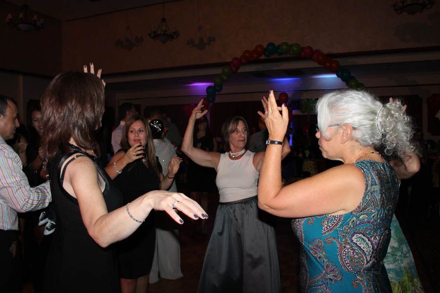 People dancing at a party under a balloon arch, some with arms raised.