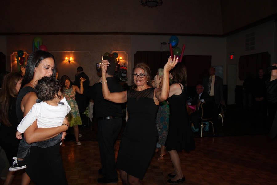 People dancing in a dimly lit hall; woman in black dress with arms raised.