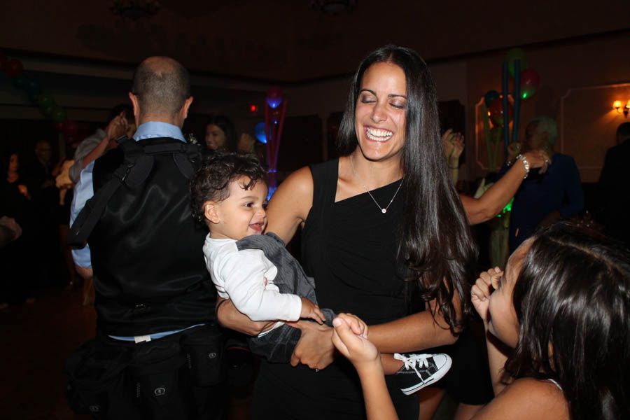 Woman dancing with a child, smiling, at a party; other people in background.