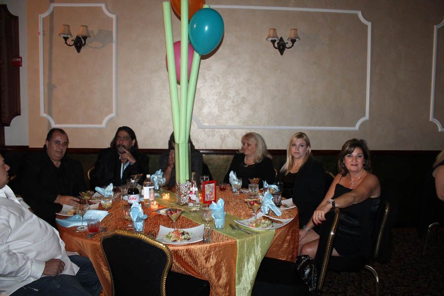 Group of people seated at a round table with food and a centerpiece; indoors, party setting.