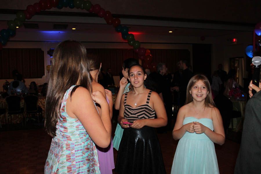 Teenagers at a formal dance, wearing dresses, with balloon decorations and dim lighting.