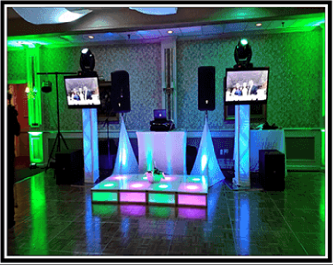 Stage setup with speakers, screens, lights, and a dance floor. Green and blue lighting illuminate the room.