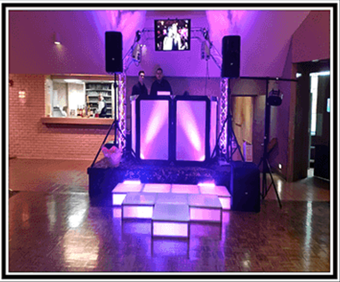 DJ setup with stage, speakers, lights, two people, and a video screen; illuminated in purple.