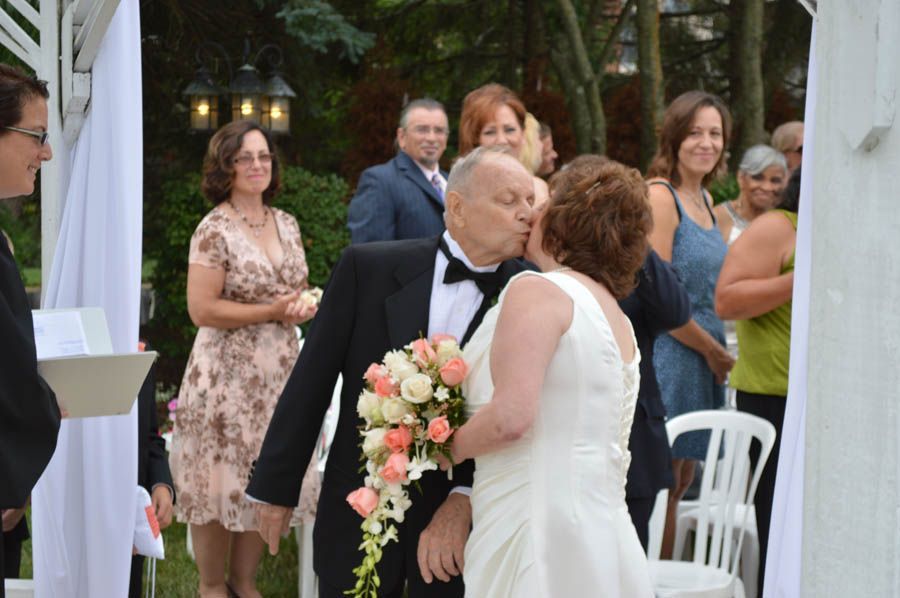 Groom kissing bride after wedding ceremony; guests watch in an outdoor setting.