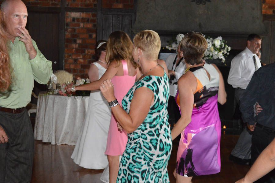 People dancing at a wedding reception. Woman in teal patterned dress, bride in white dress.