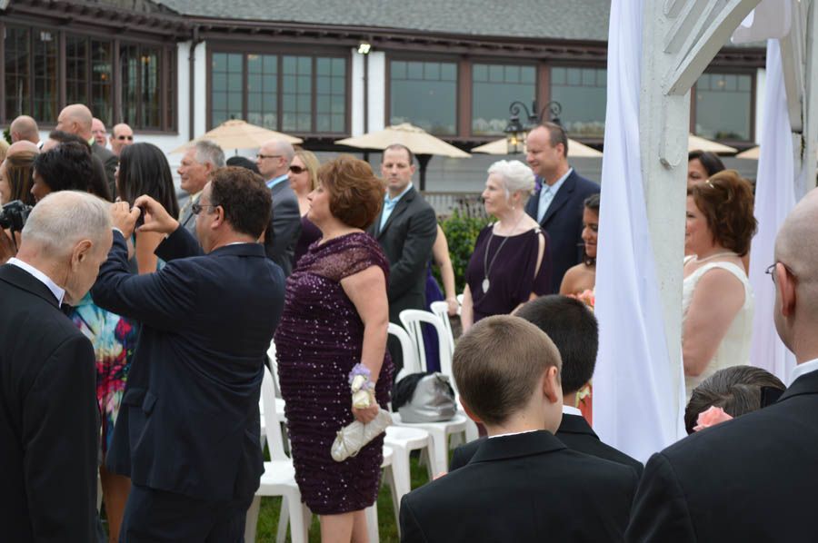 People at an outdoor wedding ceremony; several guests looking on and taking pictures.
