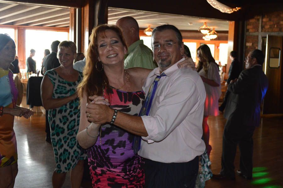 Couple dancing at an event, woman in colorful dress, man in pink shirt and tie, smiles, indoors.