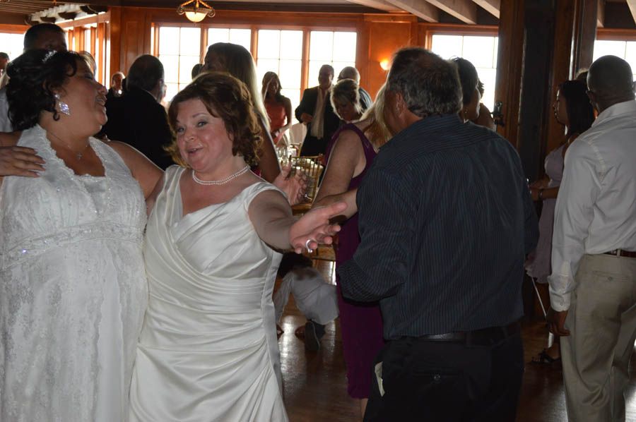 Two women in wedding dresses dance with other guests at a reception.