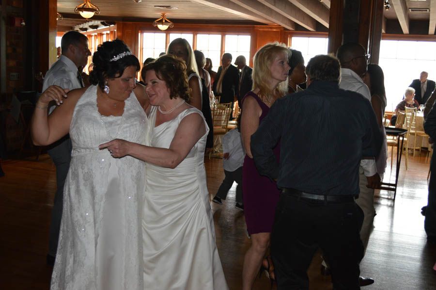 Two women in wedding dresses dance at a reception; others dance and socialize.