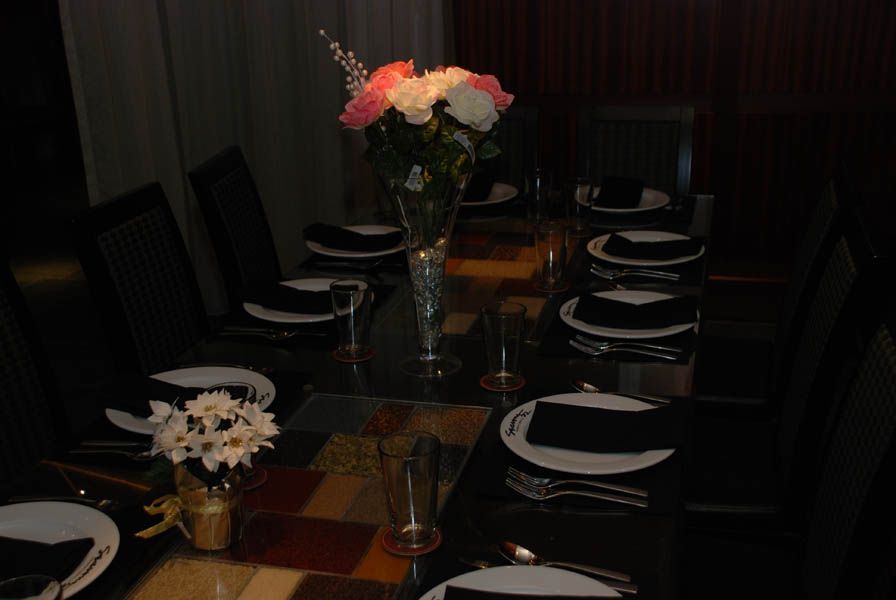 A table set for a meal with plates, silverware, black napkins, and flower arrangements in a dark room.