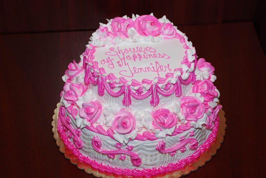 Two-tiered cake with pink and white frosting, decorated with roses, saying 