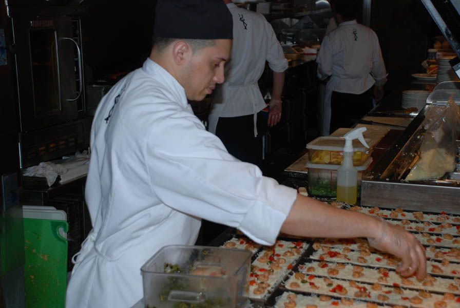 Chef in white coat and hat arranging food on a tray in a commercial kitchen.