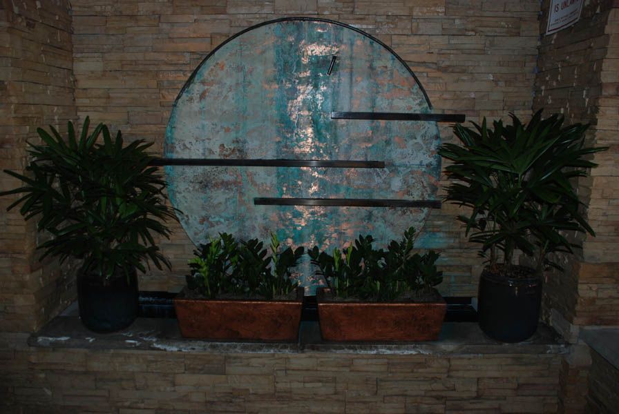 Green plants with brown pots, set against a teal and brown circular backdrop on a brick wall.
