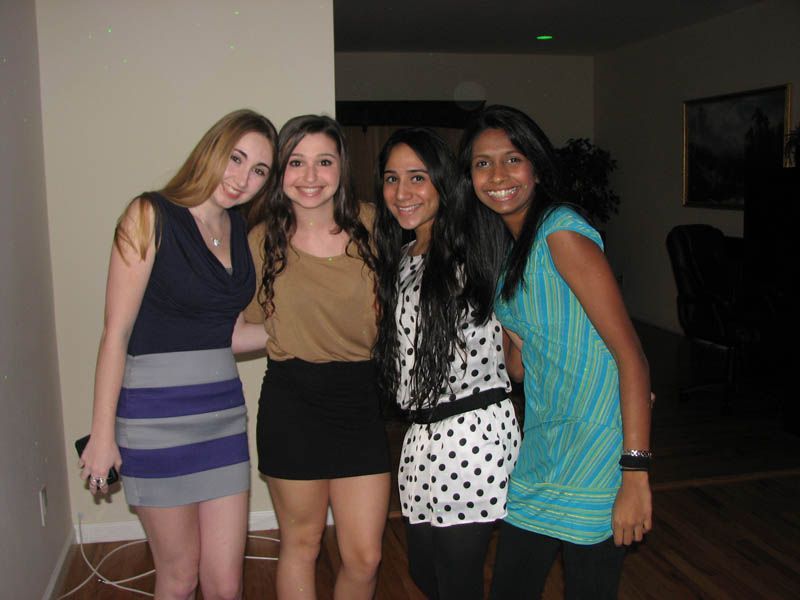 Four young women smiling, posing closely together in an indoor setting.