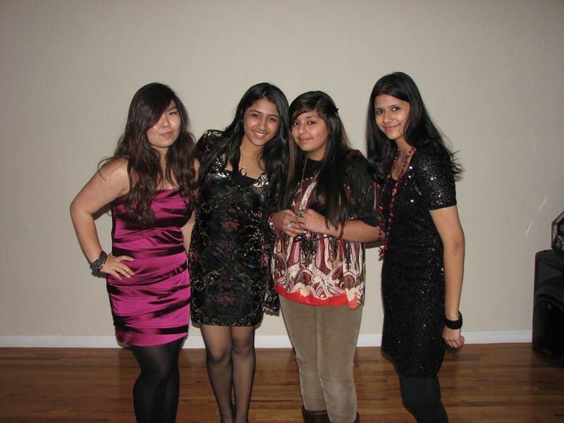 Four people pose together for a photo in a room. One person wears a pink dress. Others wear dark tops and pants.