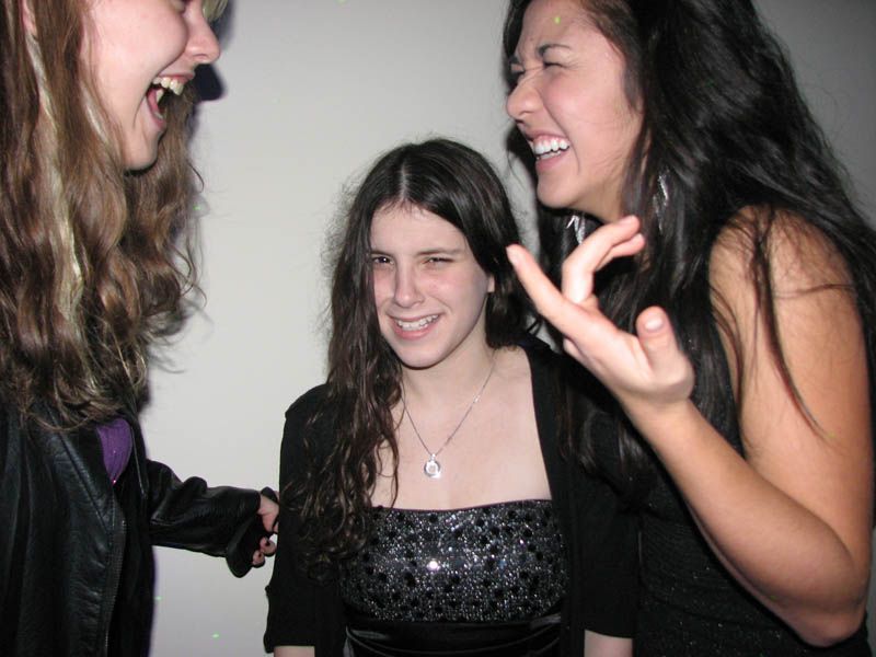 Three smiling people indoors; one is wearing a sparkly dress, the others are laughing.