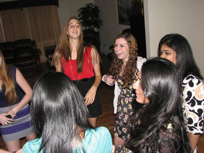Young women laughing and dancing together indoors at a party.