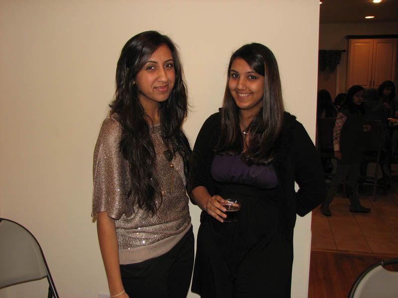 Two women smiling, posing for a photo. One in a sequined top, the other in a black top holding a drink.