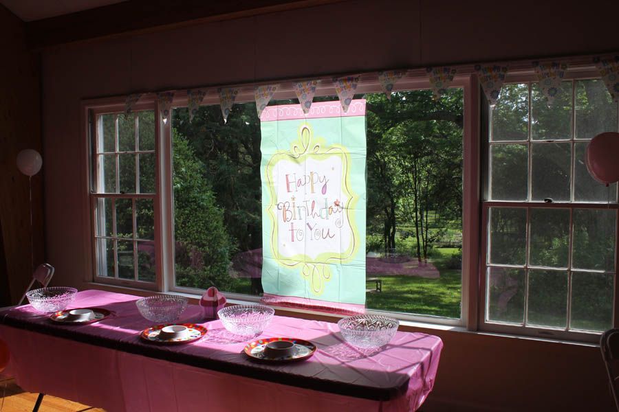Pink table with bowls and plates in front of a window with a banner reading “Happy Mother’s Day” and a backyard view.