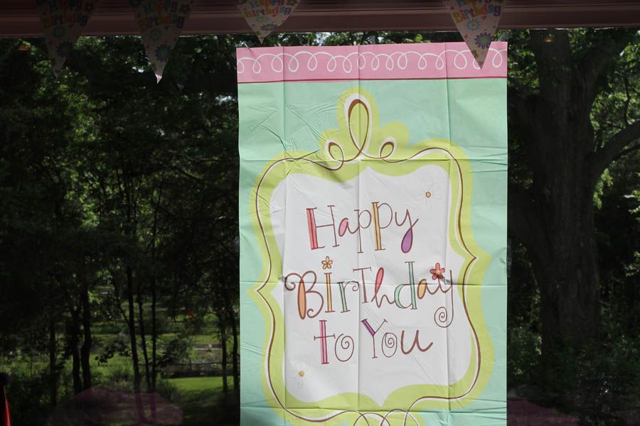 Happy birthday banner, pastel colors, outdoors with trees in the background.