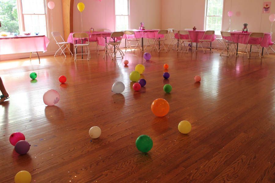 A party room with pink tables, balloons scattered on a wooden floor.