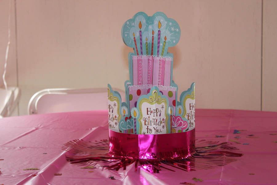 Birthday cake centerpiece on a pink tablecloth, with a pink fringe base.