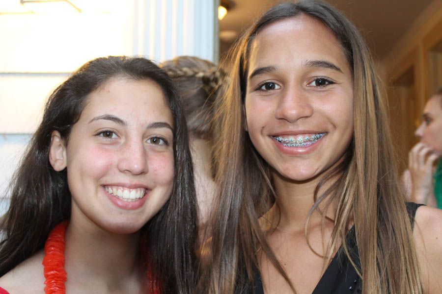 Two smiling people; one with braces, the other with a lei, near a building.