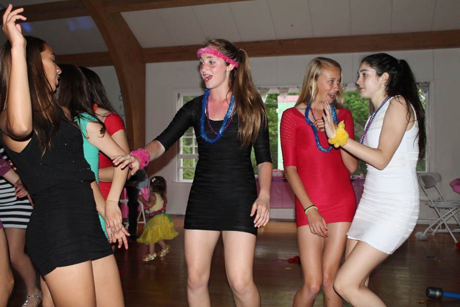 Women in short dresses dancing in a brightly lit room, some wearing accessories.
